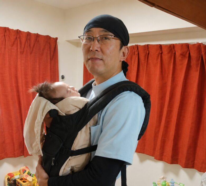 どや顔で首の座っていない赤ちゃんをサポートしながら抱っこする西川正伸